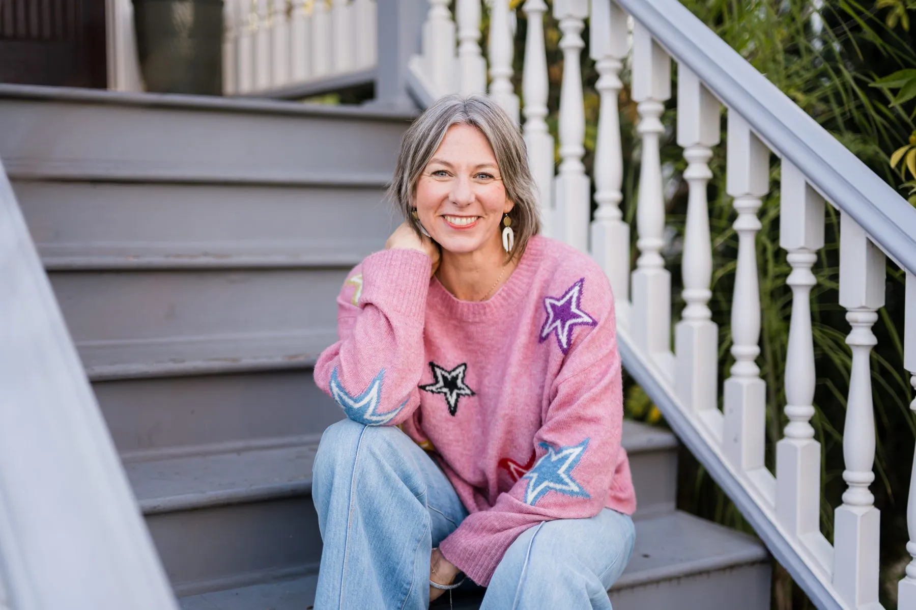 Tisha Leslie smiling, seated on outdoor stairs in a sweater patterned with stars.