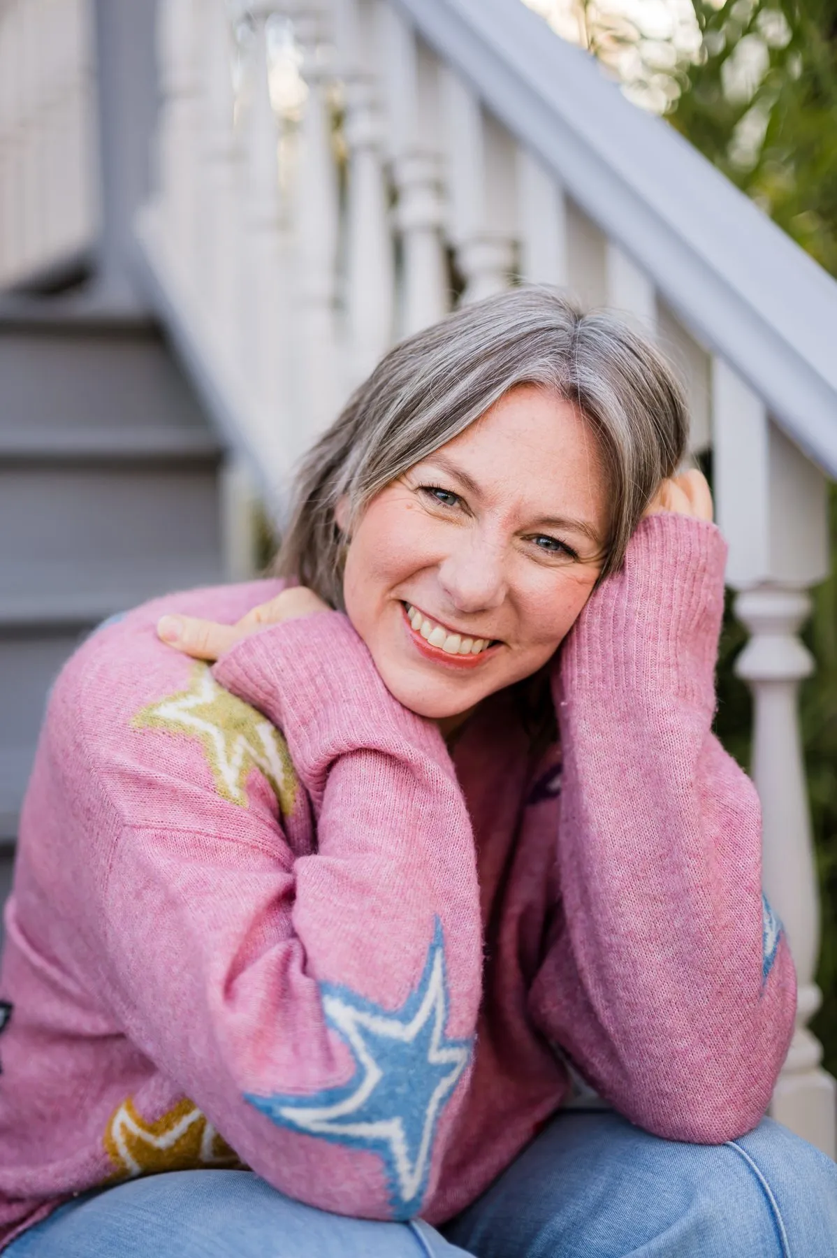 Tisha Leslie smiling, chin resting in her hands, seated on outdoor stairs in a star-patterned sweater.
